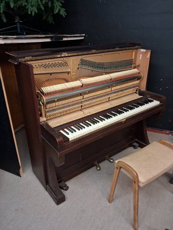 Mørkt brunt oppreist piano med frontplaten tatt av og satt til side, så hammere og dempere ligger åpent