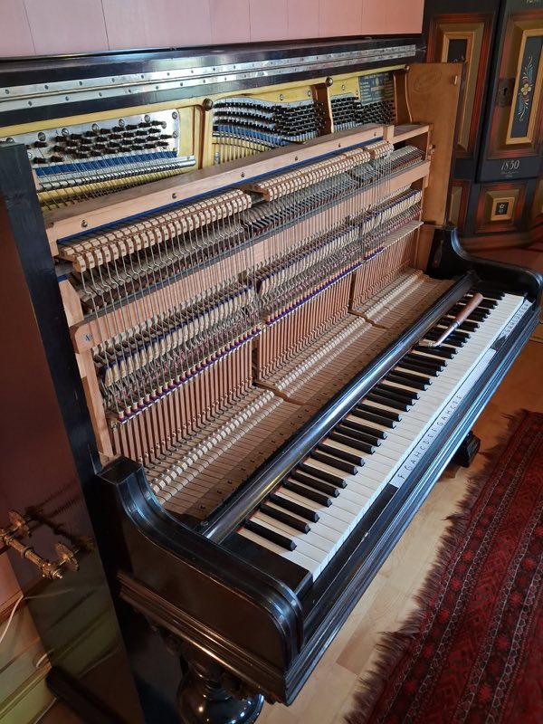 Nærbilde inn i et Blüthner-piano med panelene av — hammere, dempere og strenger synlige, med et verktøy liggende på tangentene